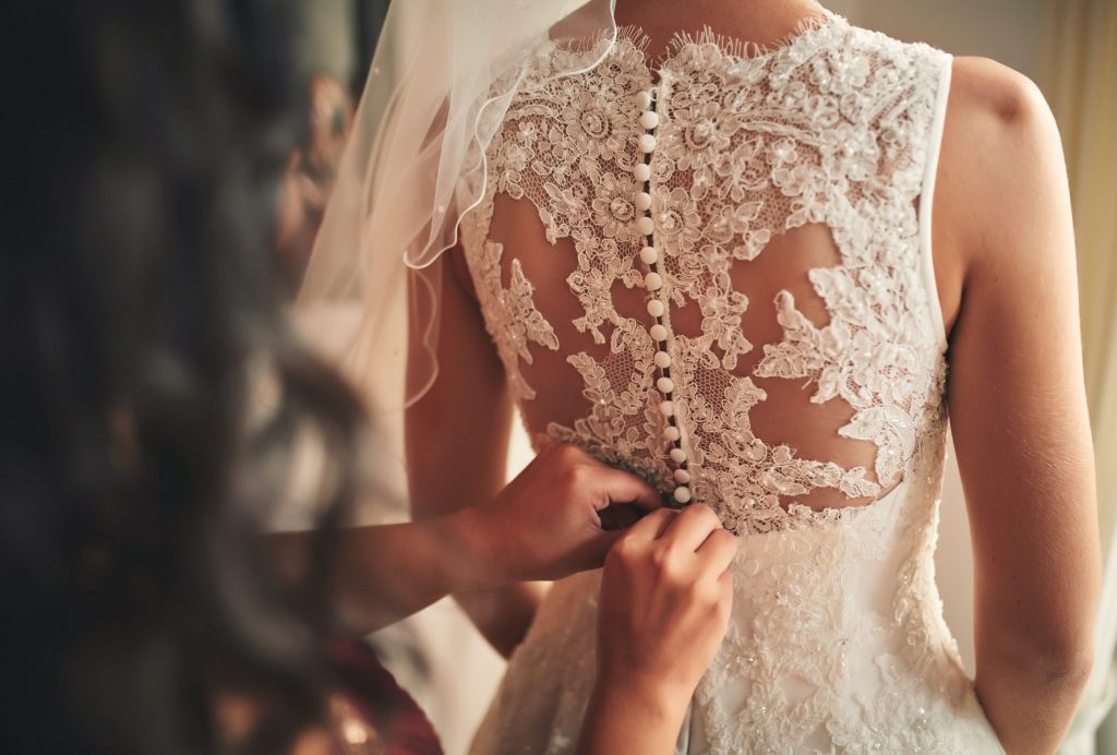 Bridesmaid helping bride fasten corset close-up and getting her dress, preparation concept in morning for wedding ceremony.